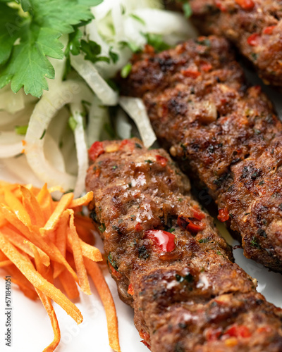 Lula kebab with side dish of fresh vegetables on white plate. Asian cuisine, Oriental cuisine. Minced meat products. Pickled onions and carrots. Close-up. Soft focus. View from above.