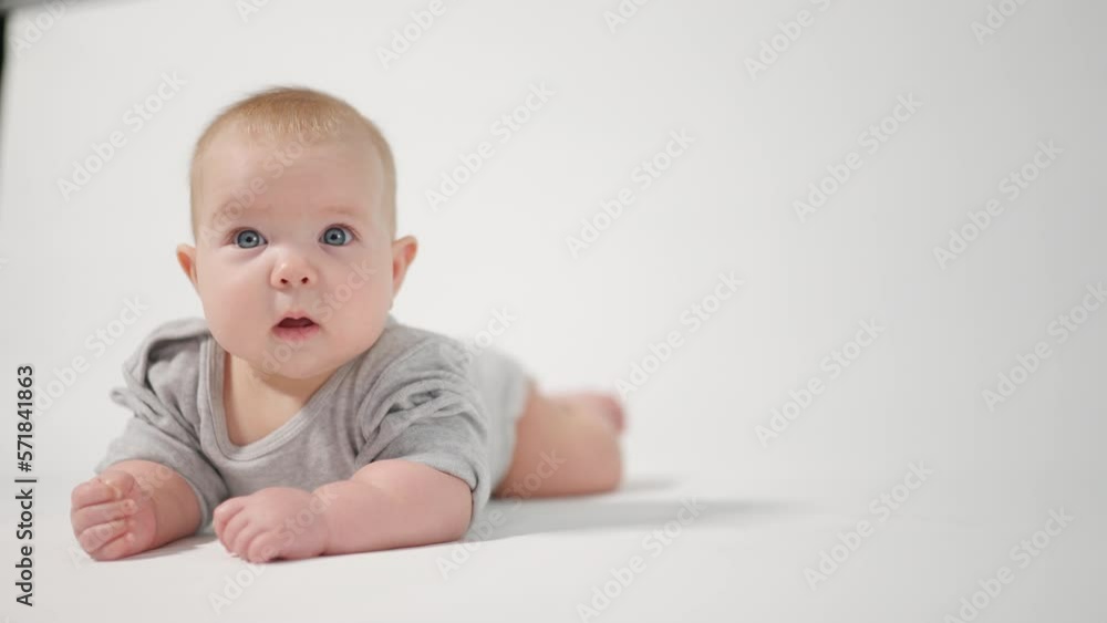 Portrait of a baby. A baby lying on his stomach in close-up against a white background, looking at the cameraman Portrait of a baby. A baby lying on his stomach in close-up against a white background, looking at the cameraman