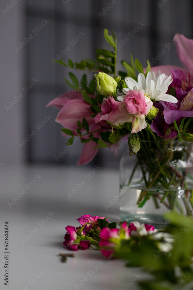 Flowers in a glass vase on a white table. Bouquet of alstroemeria, orchids, roses and white chrysanthemums.
