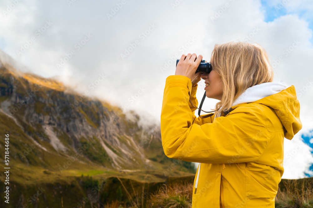 Young blonde woman hiking in mountains in the Giau Pass and looking through binoculars. Wanderlust concept. Young blonde woman hiking in mountains in the Giau Pass and looking through binoculars. Wanderlust concept.