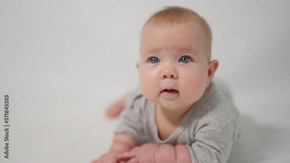 Portrait of a baby. A baby lying on his stomach in close-up against a white background, looking at the cameraman Portrait of a baby. A baby lying on his stomach in close-up against a white background, looking at the cameraman