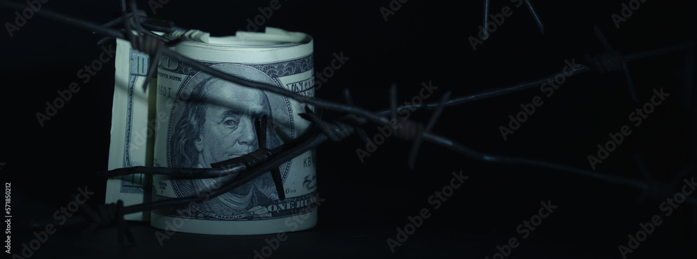 Close up barbed wire against US Dollar bill as symbol of economic warfare, sanctions and embargo busting. Selective focus. Horizontal image.