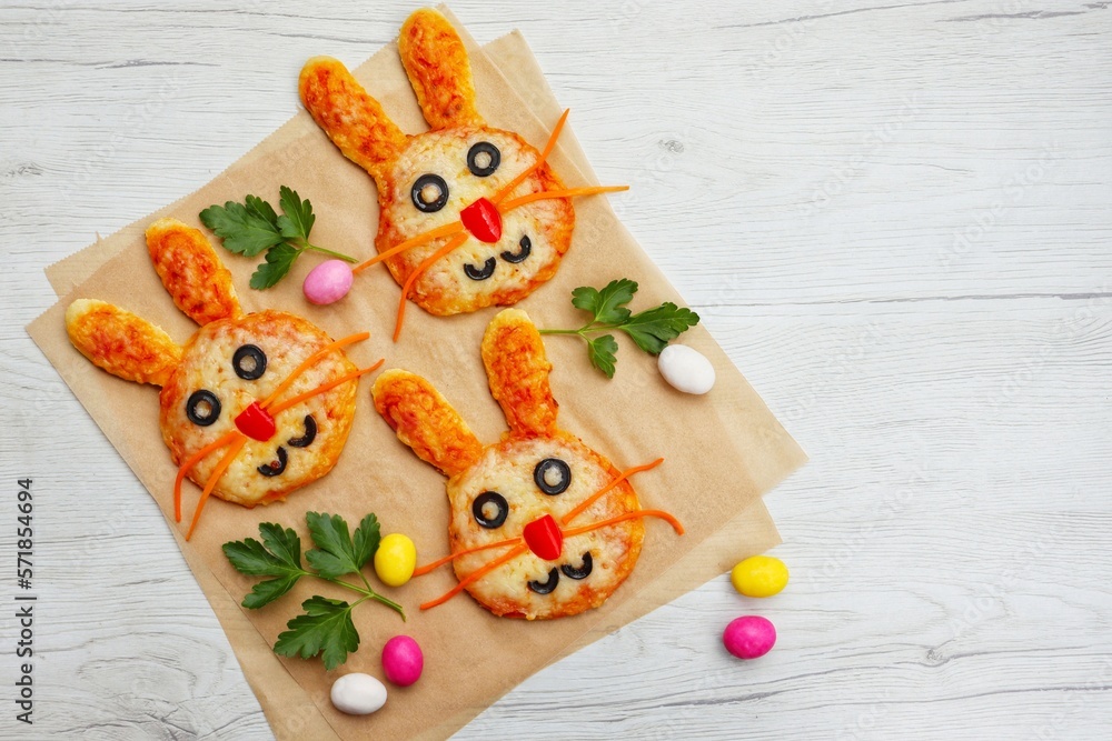 Selective focus on mini easter bunny pizzas on parchment paper with white wood background.Art food idea for kids Easter's party.Top view.Copy space
