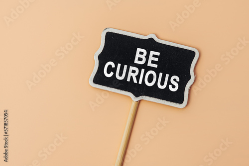 Be Curious - text on a small chalkboard on a beige background. Top view. Communication and brainstorming