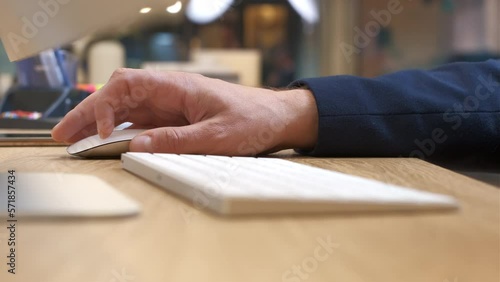 Man scrolls and clicks the white mouse. The manager's hand in a suit. The concept of successful business tasks. Gadgets with modern design. Office interior with a bright desk. Close-up, side view.
