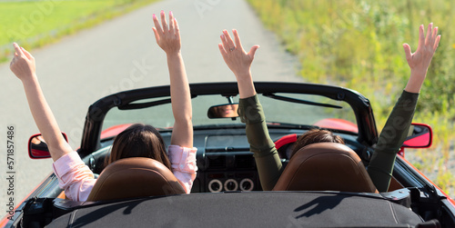 Cuadro en lienzo Back view of happy girls driving red cabriolet car with raised hands during vacation road trip having fun together discovering new places
