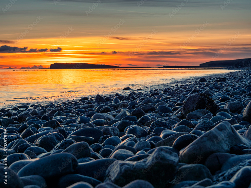 Obraz premium Colorful sunset over ocean, rough stone coast in foreground. Warm and cool color. Salthill beach, Galway city, Ireland. Selective focus. Nature scene with rich orange and blue color.