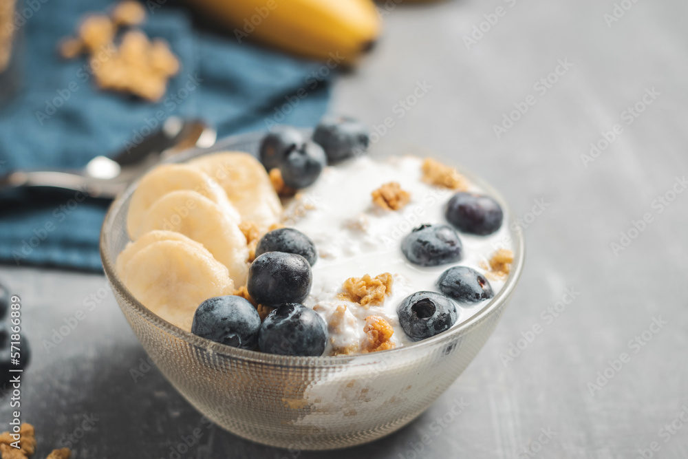 Granola cereal oatmeal with white yogurt, blueberries and banana fruits in a bowl on a blue napkin, grey background Granola cereal oatmeal with white yogurt, blueberries and banana fruits in a bowl on a blue napkin, grey background