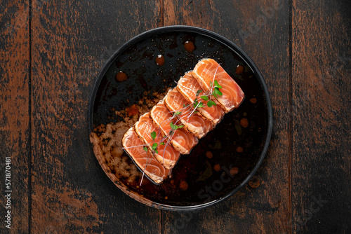 Fresh salmon fillet cut into pieces on a plate with soy sauce. Asian dish sashimi from raw salmon, top view on wooden table