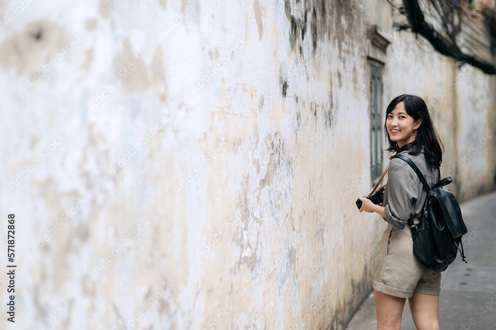 Young Asian woman backpack traveler using digital compact camera, enjoying street cultural local place and smile. Traveler checking out side streets.