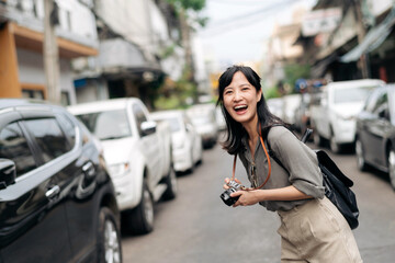 Young Asian woman backpack traveler using digital compact camera, enjoying street cultural local place and smile. Traveler checking out side streets.
