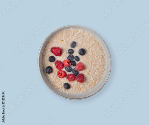 Oatmeal porridge with raspberries and blueberries in a bowl on a blue background. The concept of a dietary, healthy and nutritious breakfast.