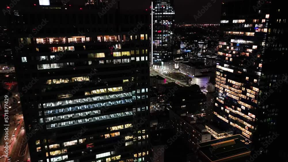 Close up aerial view to a skyscraper City center District at the night. Camera moving up high around the building showing illuminated offices inside and beautiful city panorama on the background. Close up aerial view to a skyscraper City center District at the night. Camera moving up high around the building showing illuminated offices inside and beautiful city panorama on the background.