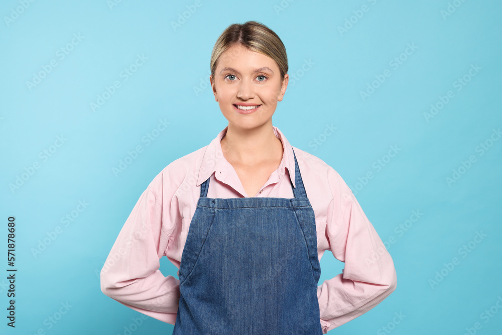 Beautiful young woman in denim apron on light blue background Beautiful young woman in denim apron on light blue background