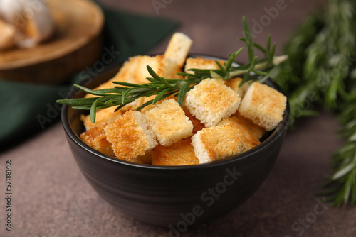 Delicious crispy croutons and rosemary in bowl on dark table, closeup