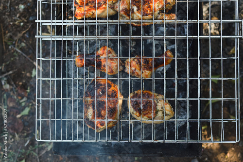 Outdoors, top view of a grill grate on which chicken meat with a golden crust is baked on charcoal and fire, copy space.