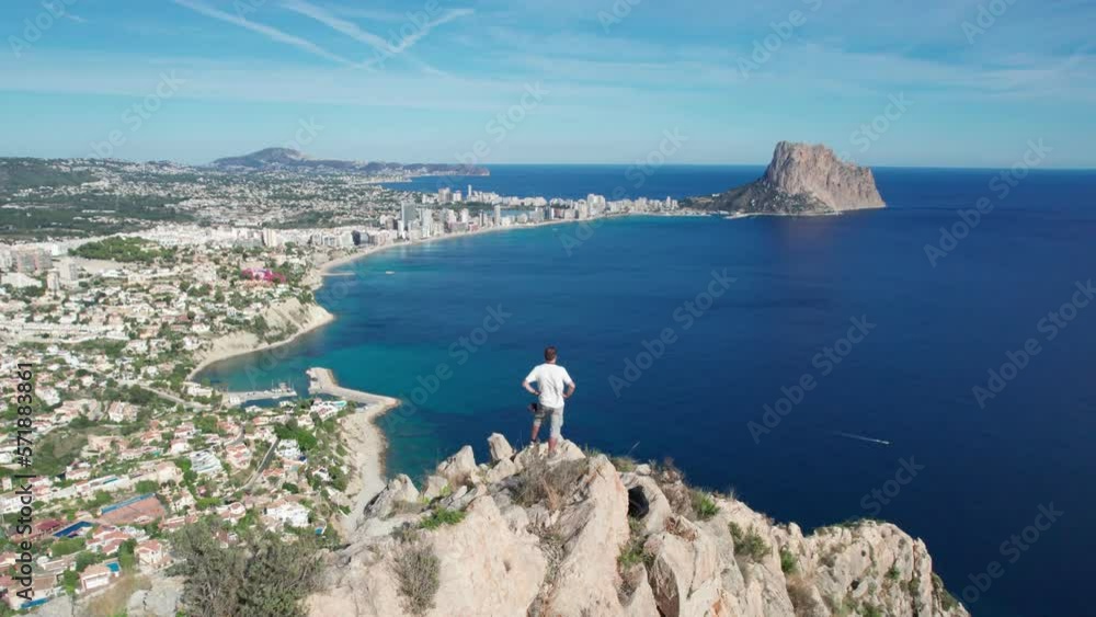A man stands on the edge of a cliff overlooking the ocean. Tourist on top of the mountain with seascape. Success victory achievement concept. A man stands on the edge of a cliff overlooking the ocean. Tourist on top of the mountain with seascape. Success victory achievement concept.