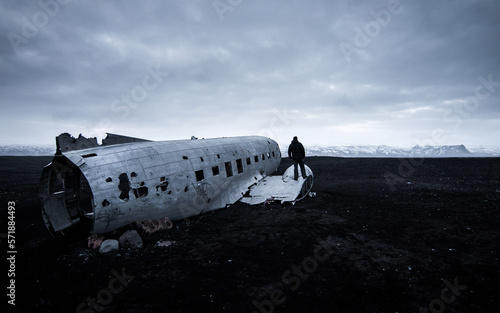 Image of the downed and abandoned plane in Sólheimasandur, Iceland, with a person standing on top enjoying the black sand landscape.