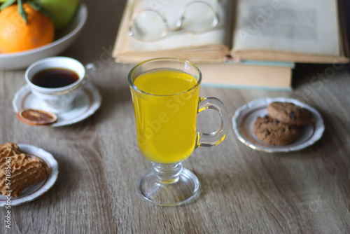 Cup of tea  plates with cookies  glass of orange juice  books  reading glasses  bowl of fruit and candles on the table. Selective focus.