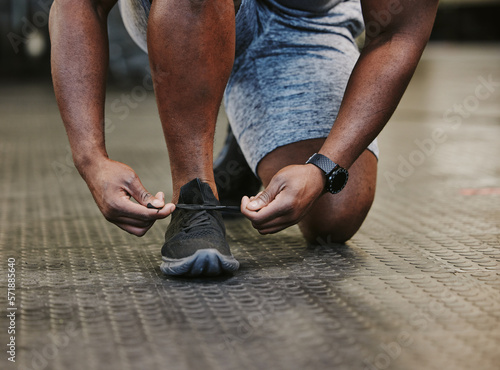 Hands, fitness and tie shoes in gym to start workout, training or exercise for wellness. Sports, athlete health and black man tying sneakers or footwear laces to get ready for exercising or running.