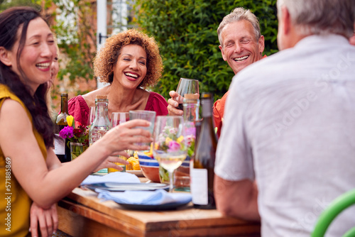 Group Of Mature Friends Talking Around Table At Summer Dinner Party In Garden At Home