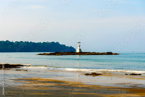 Lighthouse of white color in Khao Lak, Thailand, on the beach on a rock against the backdrop of a mountain with a cloudy and blue sky