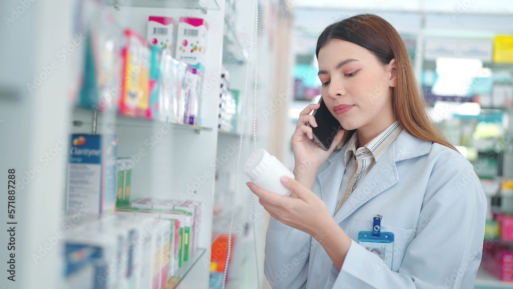 Professional asian woman pharmacist helping customer with medicine recommendation talking with customer on smartphone in drugstore