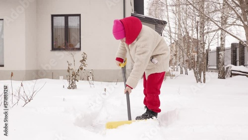 A girl cleans snow near the house. Consequences of snowfall