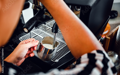 Hand of a barista in the coffee shop preparing and using a coffee machine to steam milk for a coffee menu. © NARONG