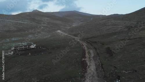 Drone Video following a rocky Mountain dirt road on Mount Olympus Greece at dusk , peaks in the distance abandoned house in the left of the frame partially cloudy photo