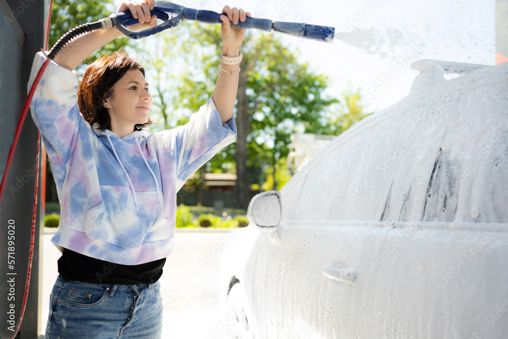 Girl washing a car in a selfservice car wash station with wahing foam