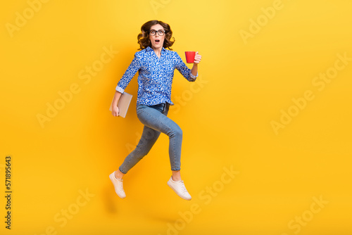 Full length profile portrait of crazy person jumping rush hold netbook coffee mug isolated on yellow color background