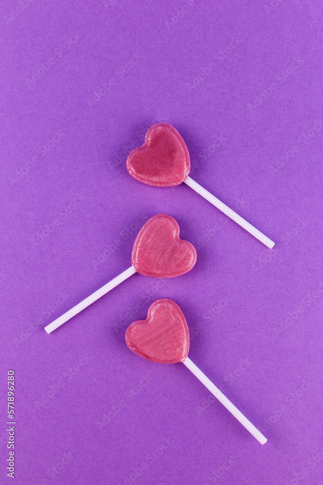 Three pink candies on stick in shape of a heart on purple background Three pink candies on stick in shape of a heart on purple background