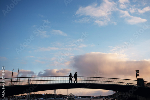 Silhouette of romantic couple walking holding hands on the bridge in the evening. Beautiful sky