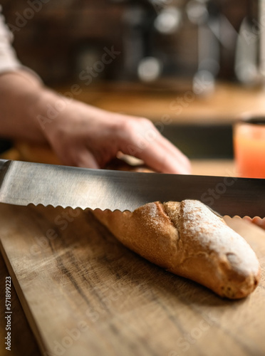 Girl hand cut french baguette with knife at kitchen. Tasty rustic fresh bread from for breakfast meal