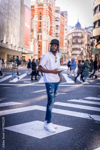 Young African American man in the city, portrait of a man with a phone at a zebra crossing with people passing in the background