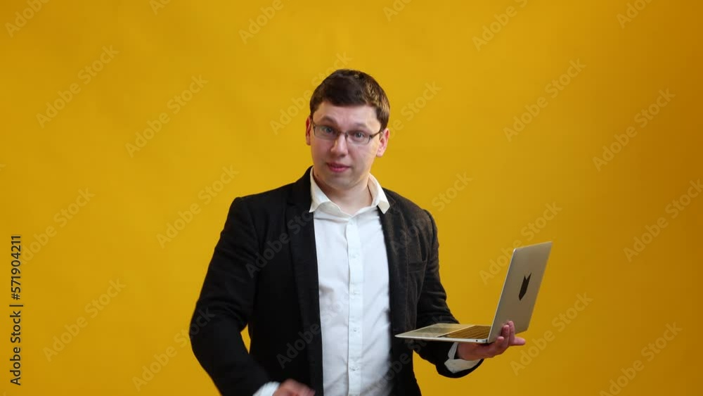 Smiling businessman speaker in glasses with laptop showing thumb up and sign OK while talking on camera over yellow studio background. Online business concept Smiling businessman speaker in glasses with laptop showing thumb up and sign OK while talking on camera over yellow studio background. Online business concept