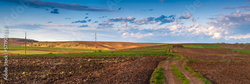 Panoramic view of plowed field prepared for sowing crops, dirt road and a hil...