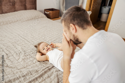 Bild auf Leinwand A father is playing peek a boo with his baby girl while she lying on the bed and laughing