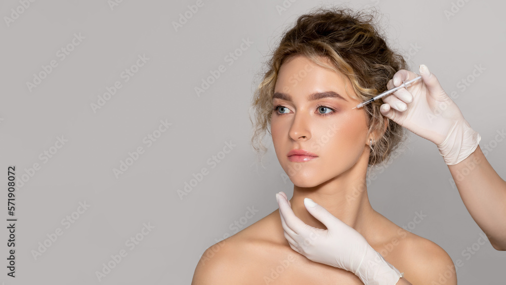 Young beautiful woman getting botox injection for eyes area, standing over grey background, panorama, copy space Young beautiful woman getting botox injection for eyes area, standing over grey background, panorama, copy space