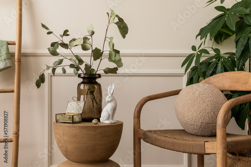 Spring composition of easter living room interior with wooden coffee table  glass vase with leaves  white bunny easter  stylish chair  round pillow and personal accessories. Home decor. Template.