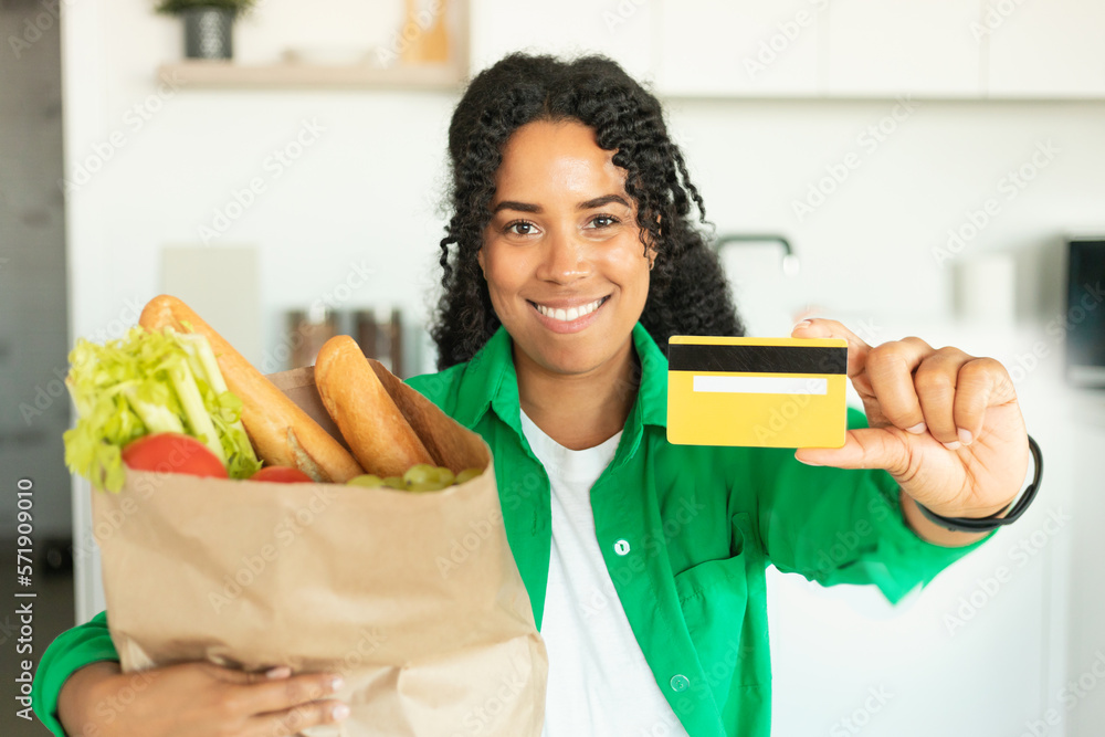 Black Woman Holding Grocery Shopping Bag Showing Credit Card Indoors Black Woman Holding Grocery Shopping Bag Showing Credit Card Indoors