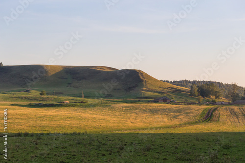 a grassy field with hill with forests in the distance. Rural scene,country road and old farm in countryside
