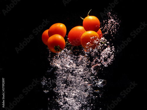 red tomatoes falling into water with splash on black background