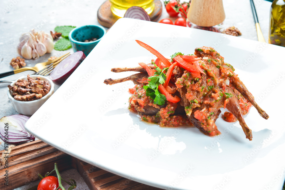 Quail baked in tomato sauce with vegetables. On a white plate. On a gray stone background. Restaurant menu. Quail baked in tomato sauce with vegetables. On a white plate. On a gray stone background. Restaurant menu.