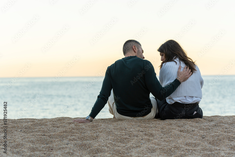 Man consoling her friend while sitting on the sand at the beach
