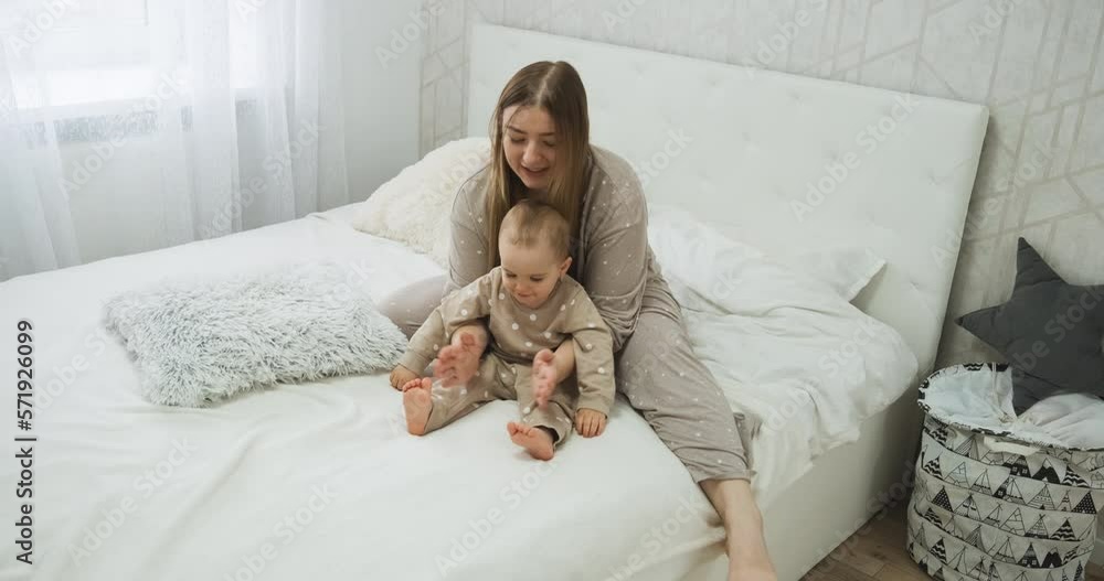 Mother in pajamas clapping hands playing with baby daughter on the bed, young mom with child in bedroom at home Mother in pajamas clapping hands playing with baby daughter on the bed, young mom with child in bedroom at home