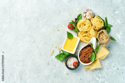 Cooking background: pesto sauce, pasta, basil, parmesan and nuts, olive oil. On a concrete background.