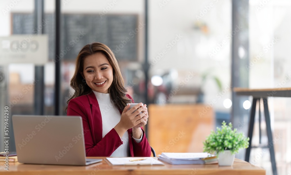 Young Asian businesswoman working and holding hot coffee cup in the office room Young Asian businesswoman working and holding hot coffee cup in the office room