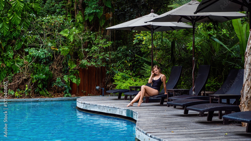Tan young model in black bikini, posing and relaxing by swimming pool